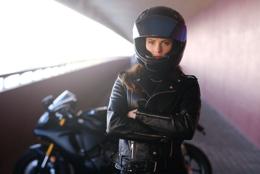 attractive serious woman is standing next to her motobike crossing hands